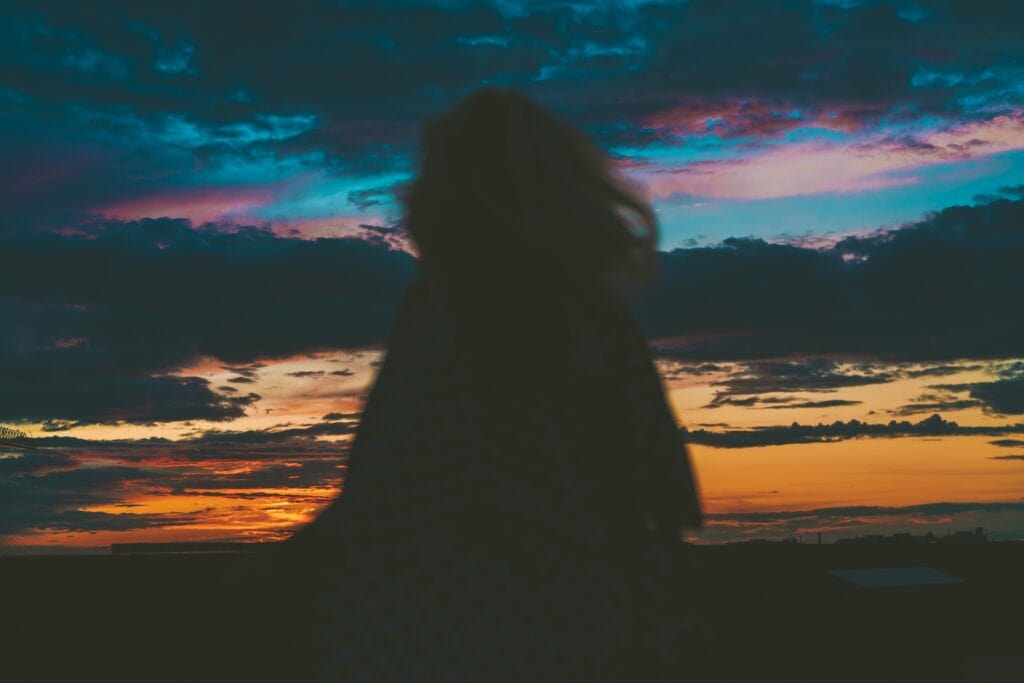 A silhouette of a person with short hair under a moody sunset sky of orange and dark blue clouds. The moody sky represents the confusion adoption can bring and the silhouette represents the isolation.