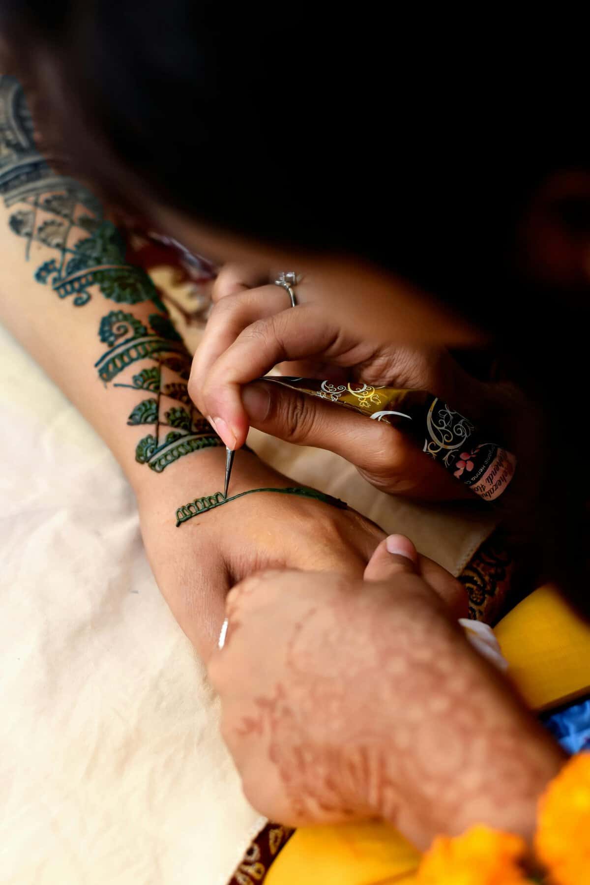 Someone applying a delicate mehendi design to someone else's arm and hand, showing the tip of the henna tube. This represents this blogs theme of intercountry adoption and cultural connection, belonging and identity.